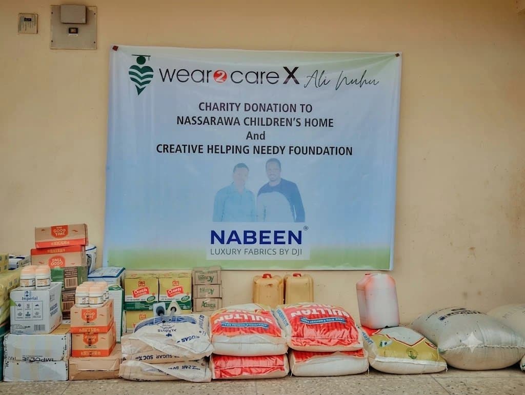 Food and household supplies donated through Wear2Care x Ali Nuhu, stacked beneath the campaign banner